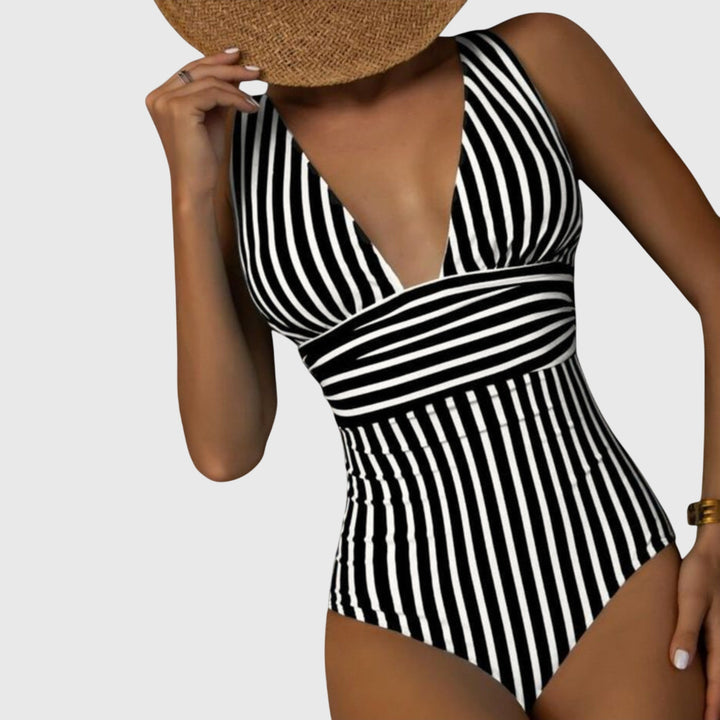 A woman walking by the sea in a bright printed swimsuit, relaxed and glowing in the sun.