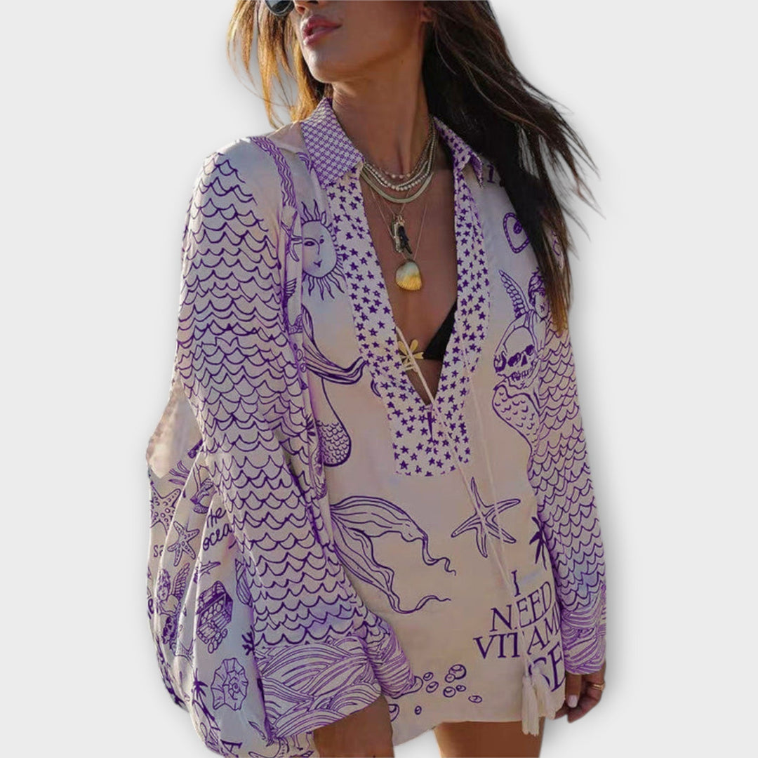 Woman walking on the beach in a relaxed tunic dress with playful maritime print and tie collar.