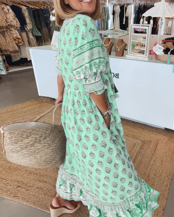 A woman wearing the Rosaleen boho beach dress with a flowing skirt, walking along the seaside.