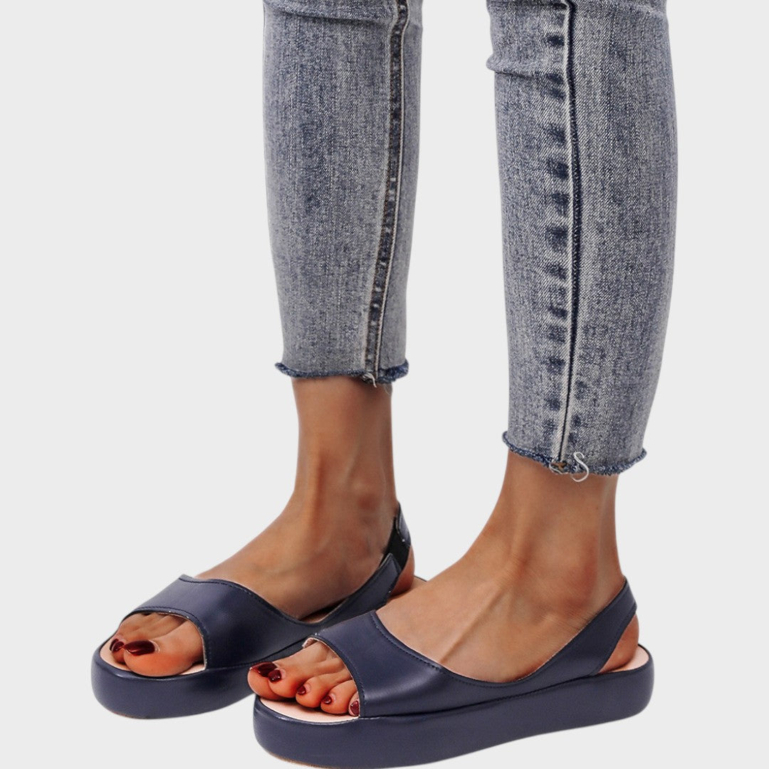 A woman walking gracefully in lightweight orthopaedic sandals with an adjustable strap on a sunny day.
