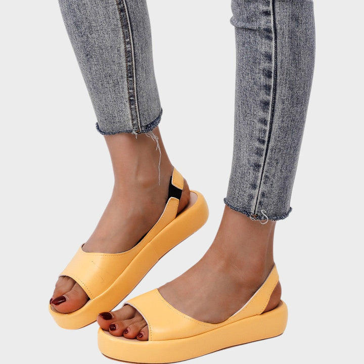 A woman walking gracefully in lightweight orthopaedic sandals with an adjustable strap on a sunny day.