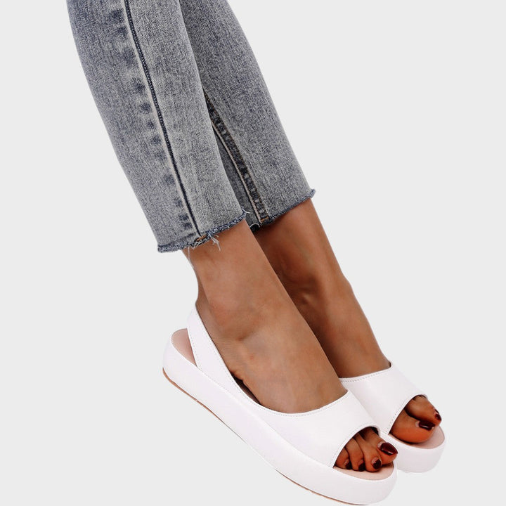 A woman walking gracefully in lightweight orthopaedic sandals with an adjustable strap on a sunny day.
