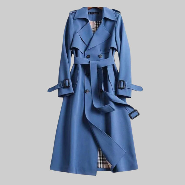 A woman wearing a belted classic trench coat with a defined waist, walking through the city.