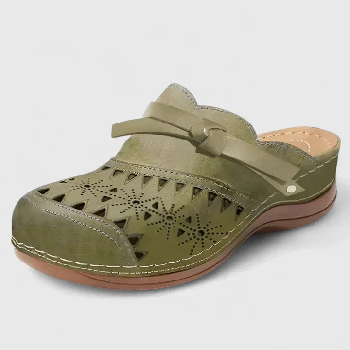 A woman slipping on airy laser-cut comfort shoes with a decorative knot detail at home.