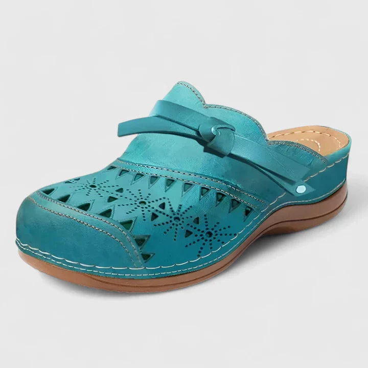 A woman slipping on airy laser-cut comfort shoes with a decorative knot detail at home.