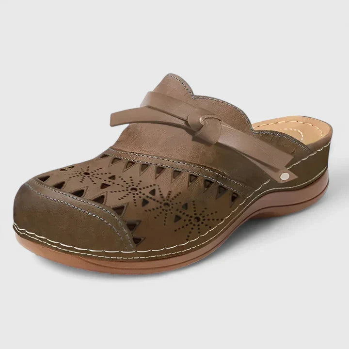 A woman slipping on airy laser-cut comfort shoes with a decorative knot detail at home.