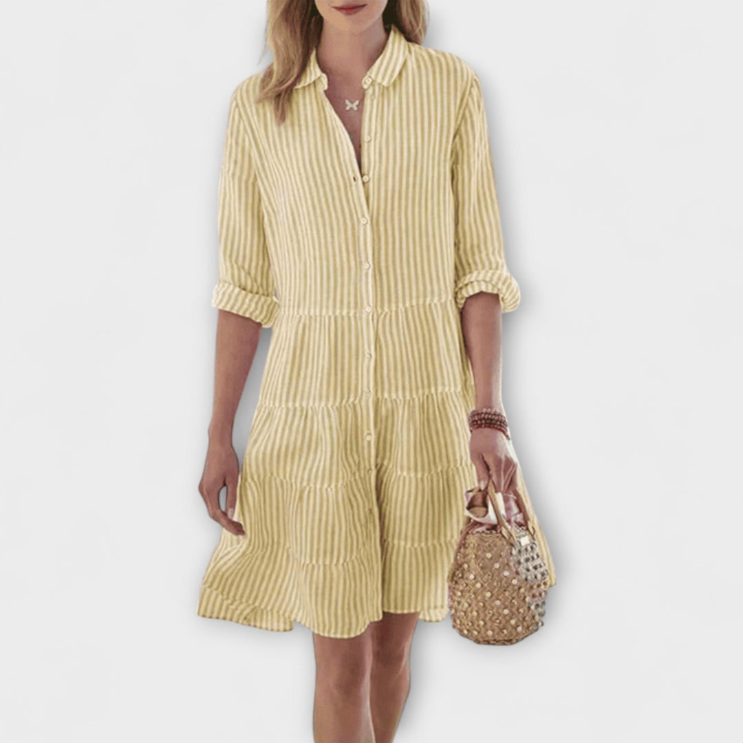 Woman wearing the Breda™ striped button-through shirt dress with roll-up sleeves, walking outdoors in the sunshine.