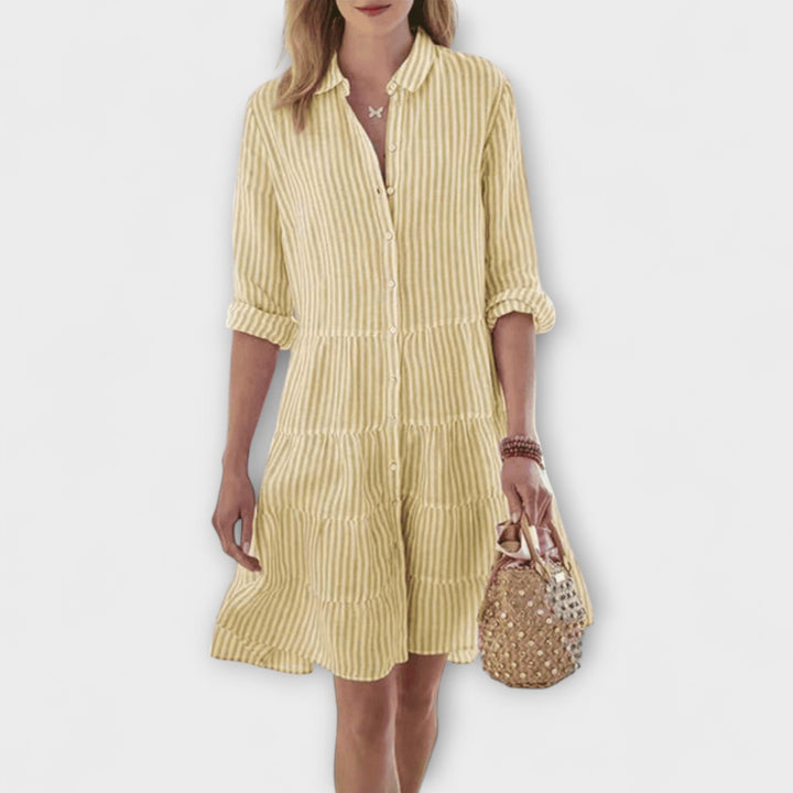 Woman wearing the Breda™ striped button-through shirt dress with roll-up sleeves, walking outdoors in the sunshine.