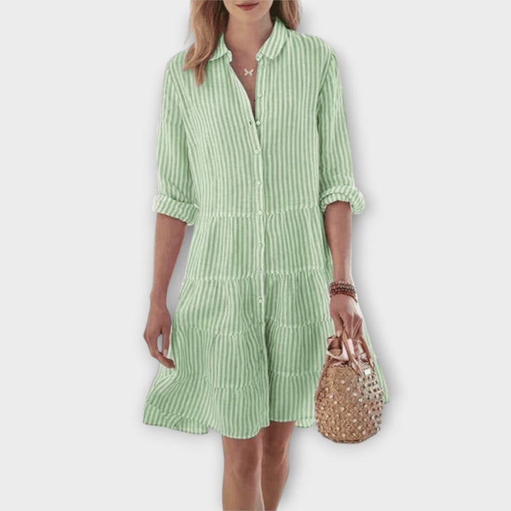 Woman wearing the Breda™ striped button-through shirt dress with roll-up sleeves, walking outdoors in the sunshine.