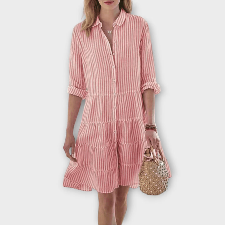 Woman wearing the Breda™ striped button-through shirt dress with roll-up sleeves, walking outdoors in the sunshine.
