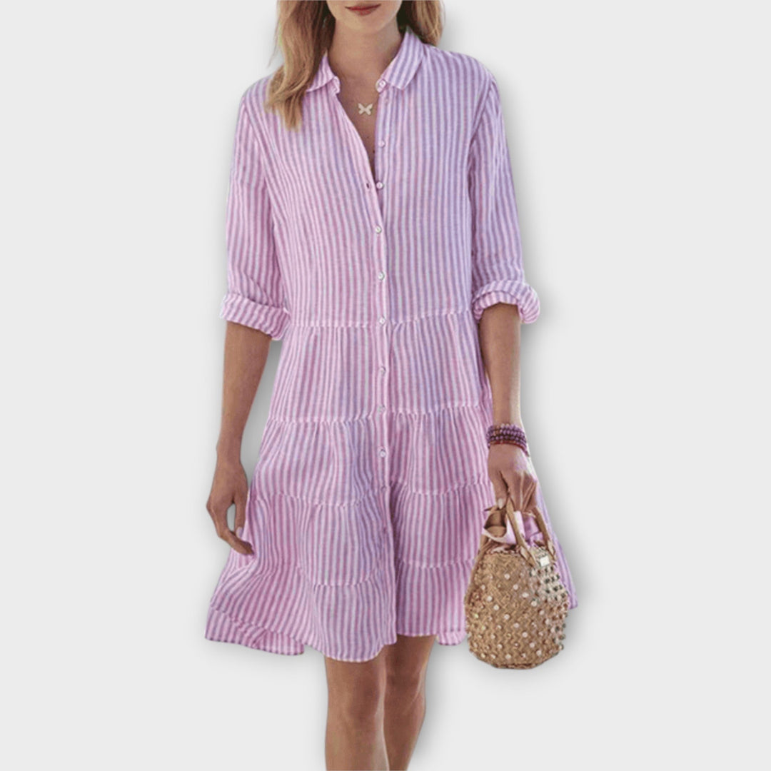 Woman wearing the Breda™ striped button-through shirt dress with roll-up sleeves, walking outdoors in the sunshine.