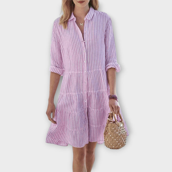 Woman wearing the Breda™ striped button-through shirt dress with roll-up sleeves, walking outdoors in the sunshine.