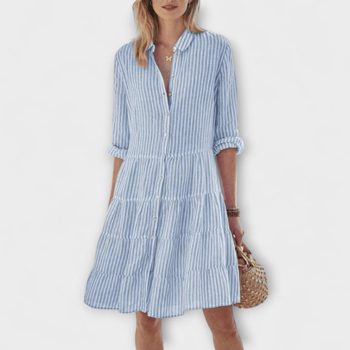 Woman wearing the Breda™ striped button-through shirt dress with roll-up sleeves, walking outdoors in the sunshine.