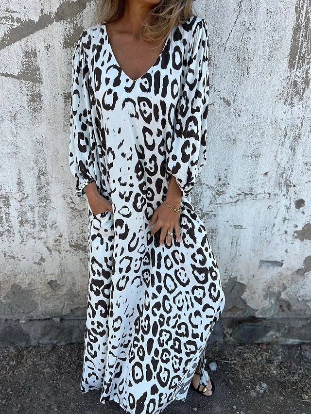 Woman in the Julia leopard print maxi dress with long sleeves and a V-neckline, walking along the shoreline.