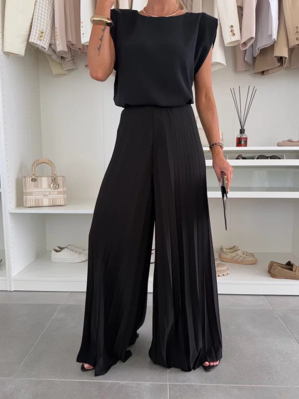 A woman wearing a structured sleeveless top with high-waisted pleated wide-leg trousers.