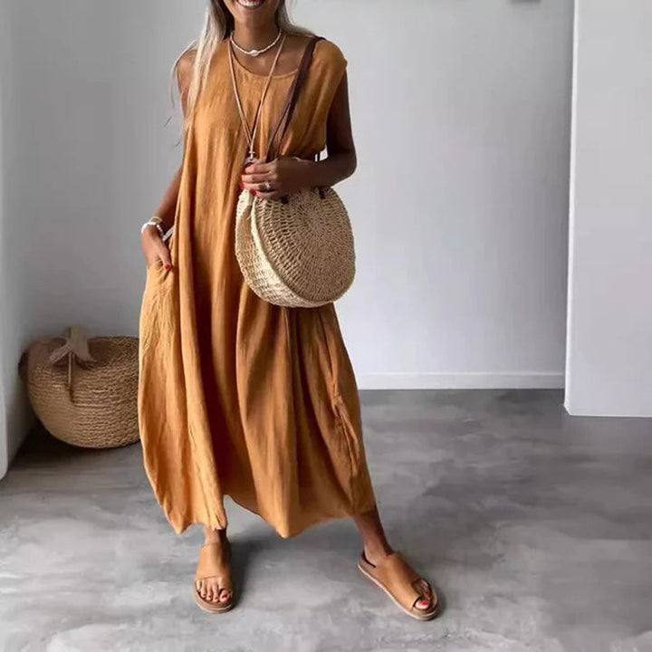 Woman wearing the Yvonne™ sleeveless flowing maxi dress with side pockets, relaxing outdoors on a warm day.
