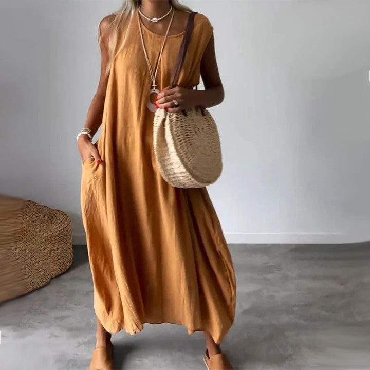 Woman wearing the Yvonne™ sleeveless flowing maxi dress with side pockets, relaxing outdoors on a warm day.