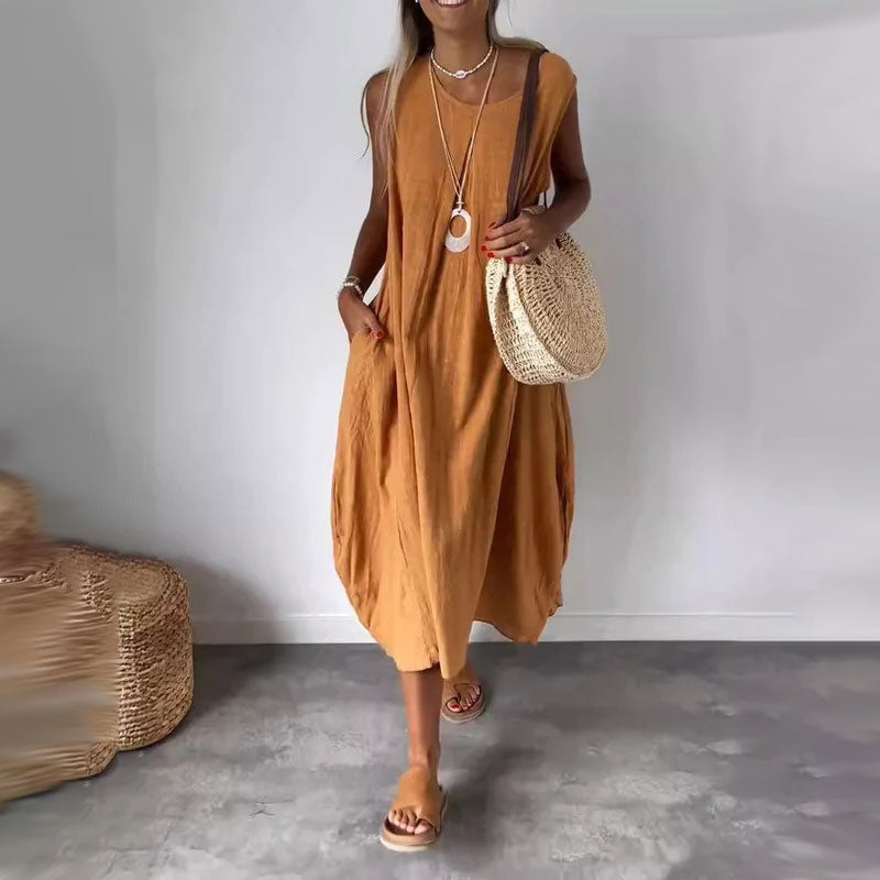 Woman wearing the Yvonne™ sleeveless flowing maxi dress with side pockets, relaxing outdoors on a warm day.