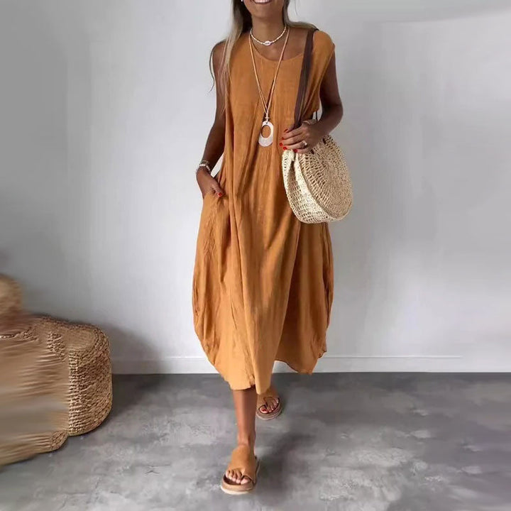Woman wearing the Yvonne™ sleeveless flowing maxi dress with side pockets, relaxing outdoors on a warm day.