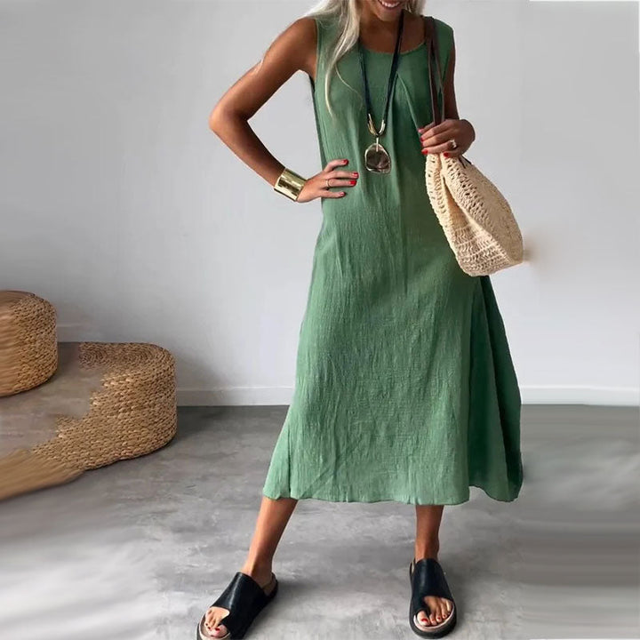 Woman wearing the Yvonne™ sleeveless flowing maxi dress with side pockets, relaxing outdoors on a warm day.