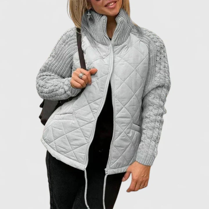 A woman wearing a patchwork hooded jacket with adjustable drawcords, hands in the pockets.