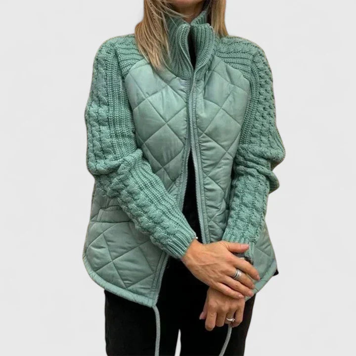 A woman wearing a patchwork hooded jacket with adjustable drawcords, hands in the pockets.