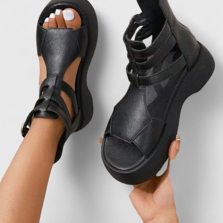 A woman stepping out in black platform sandals with crossover straps and a back zip, walking with a confident, easy stride.