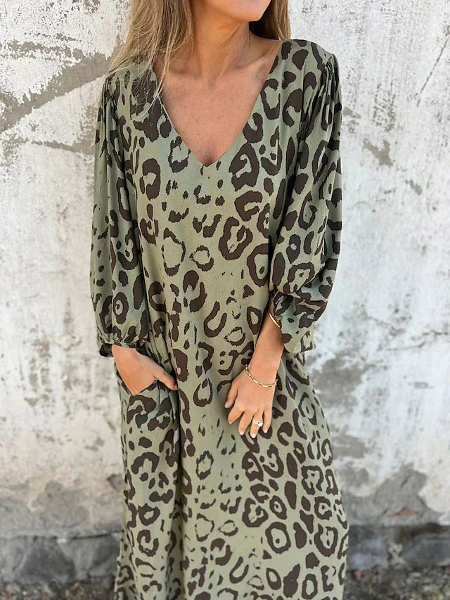 Woman in the Julia leopard print maxi dress with long sleeves and a V-neckline, walking along the shoreline.