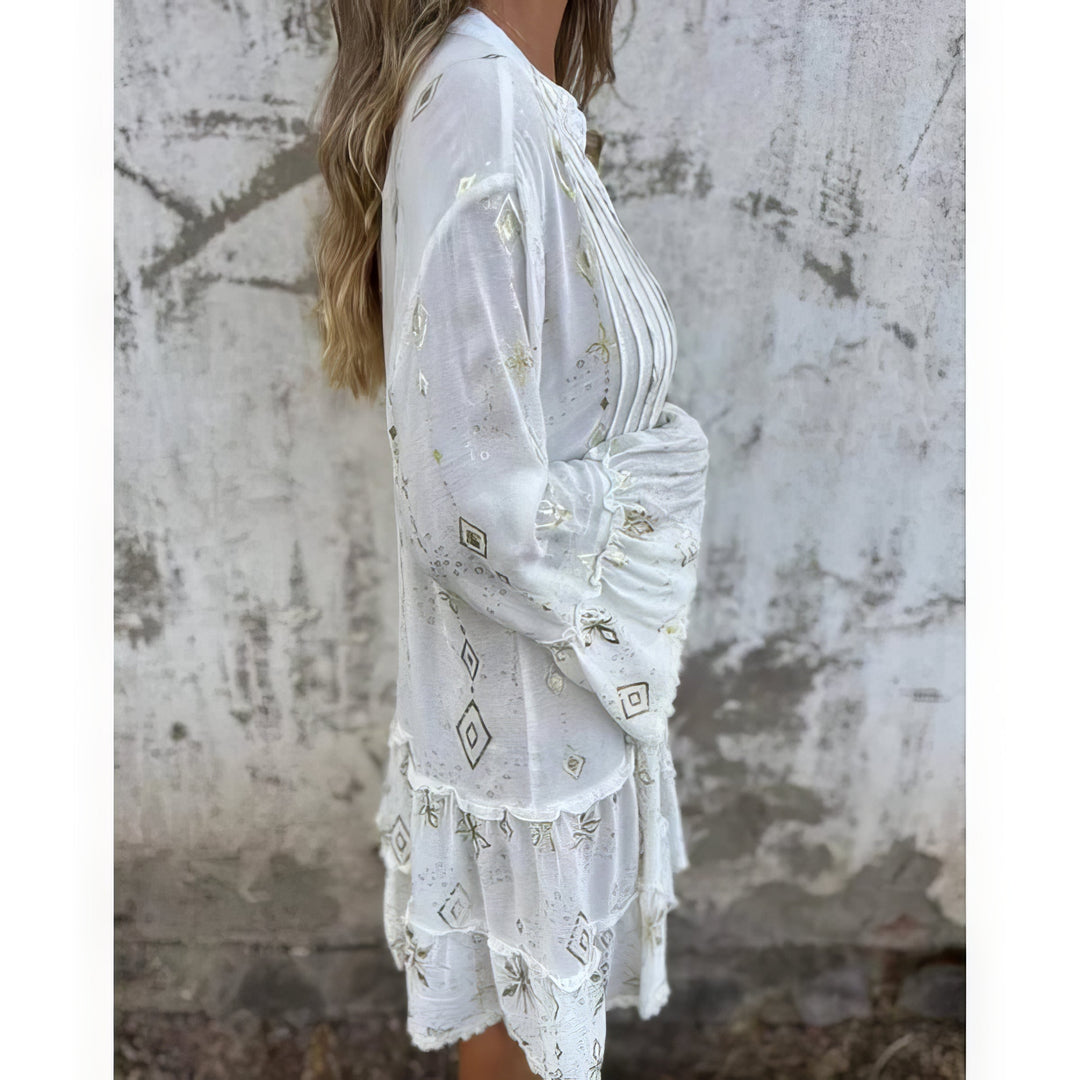 A woman wearing a black boho dress with a cream diamond-and-star print, flared sleeves and a tiered hem.