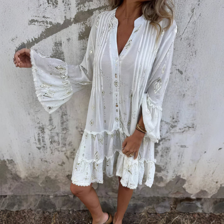 A woman wearing a black boho dress with a cream diamond-and-star print, flared sleeves and a tiered hem.