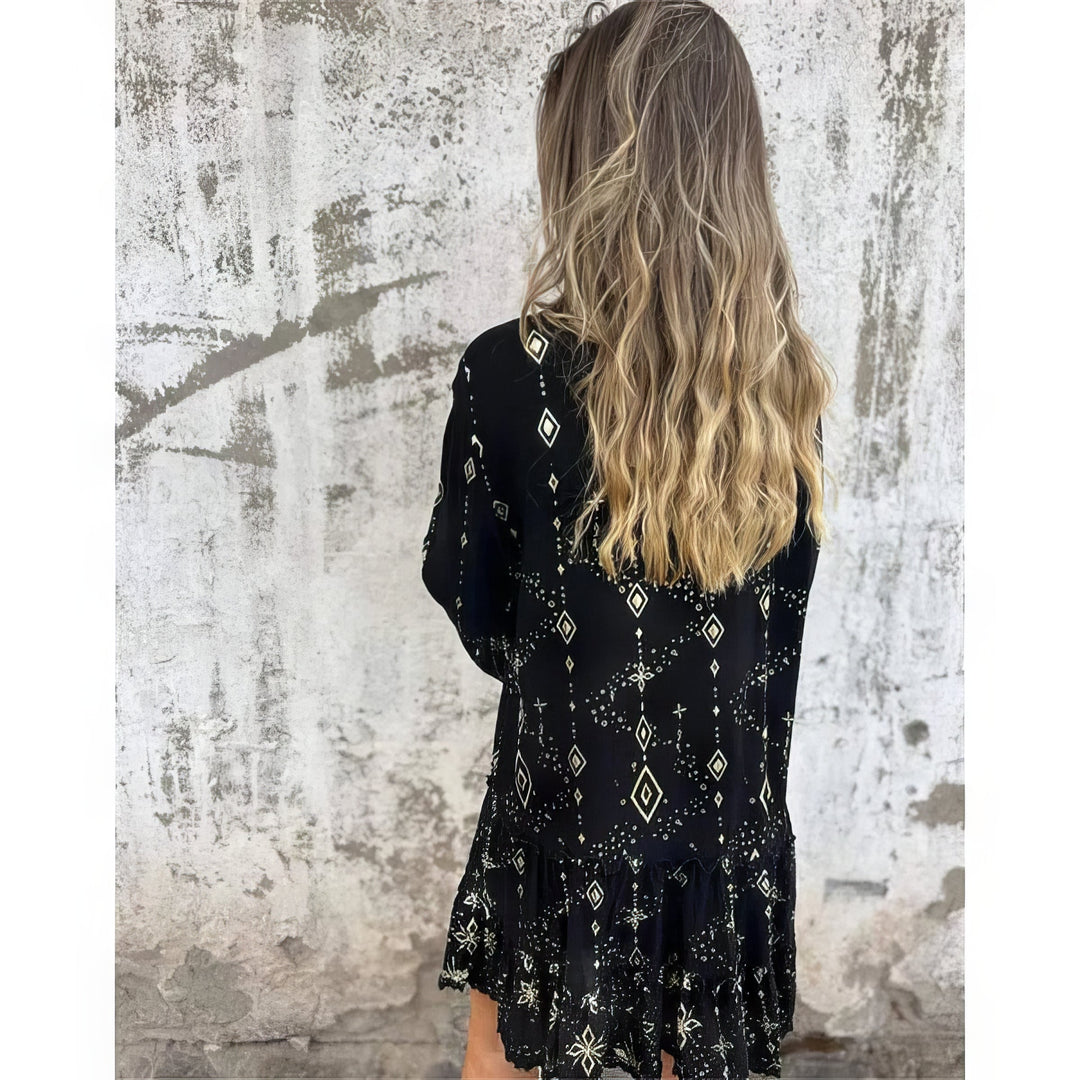 A woman wearing a black boho dress with a cream diamond-and-star print, flared sleeves and a tiered hem.