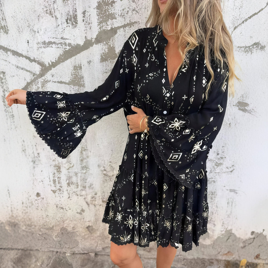 A woman wearing a black boho dress with a cream diamond-and-star print, flared sleeves and a tiered hem.