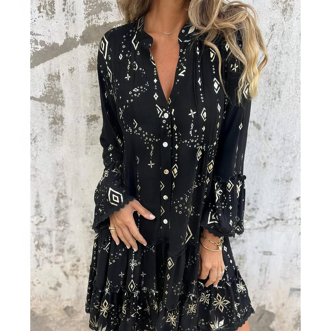 A woman wearing a black boho dress with a cream diamond-and-star print, flared sleeves and a tiered hem.