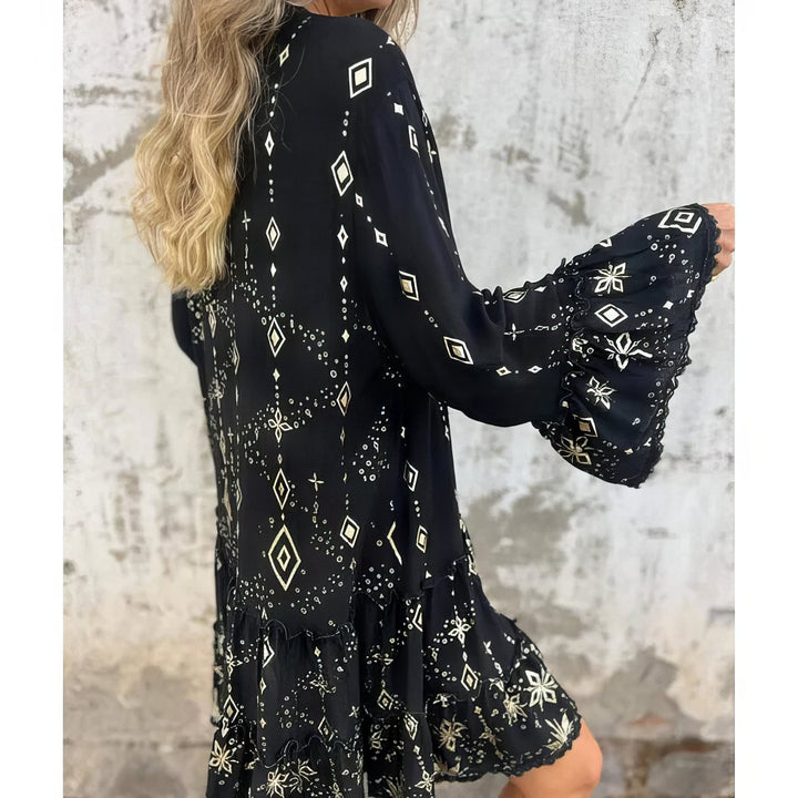 A woman wearing a black boho dress with a cream diamond-and-star print, flared sleeves and a tiered hem.