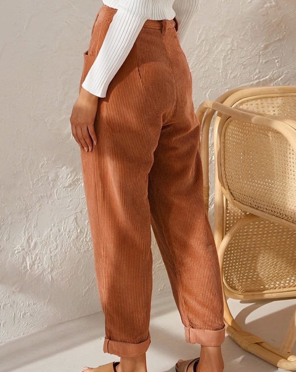 Woman wearing loose high-waisted trousers with a tucked-in top, standing in soft light.