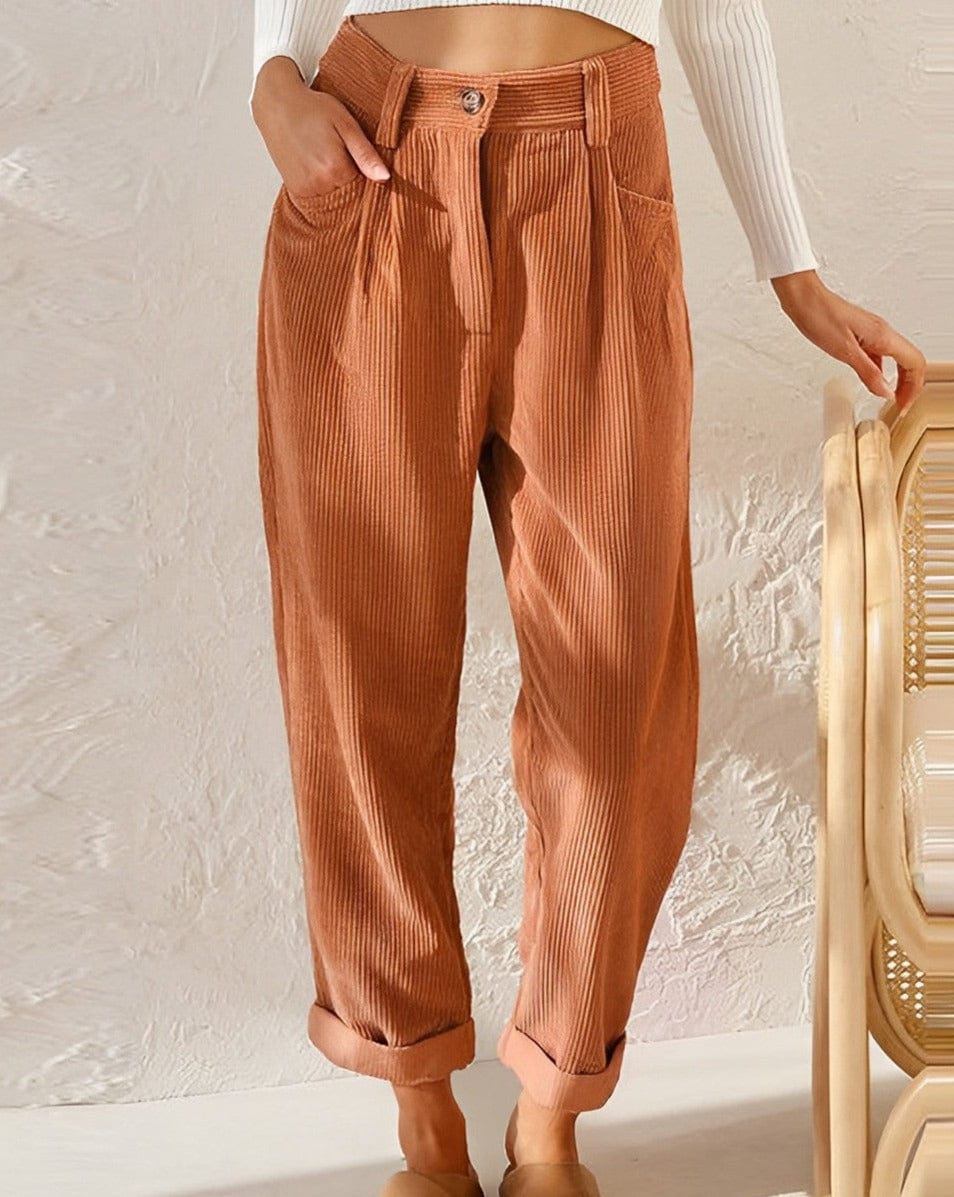 Woman wearing loose high-waisted trousers with a tucked-in top, standing in soft light.